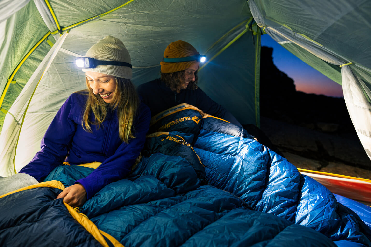 Two campers wearing headlamps inside a tent with Sea to Summit sleeping bags